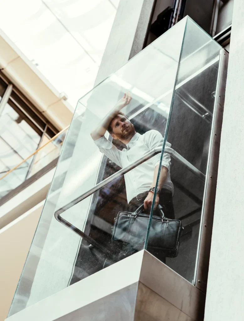 Businessman in glass elevator holding briefcase and looking upwards.