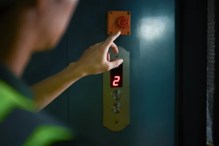 Elevator technician pressing red emergency stop button inside lift.
