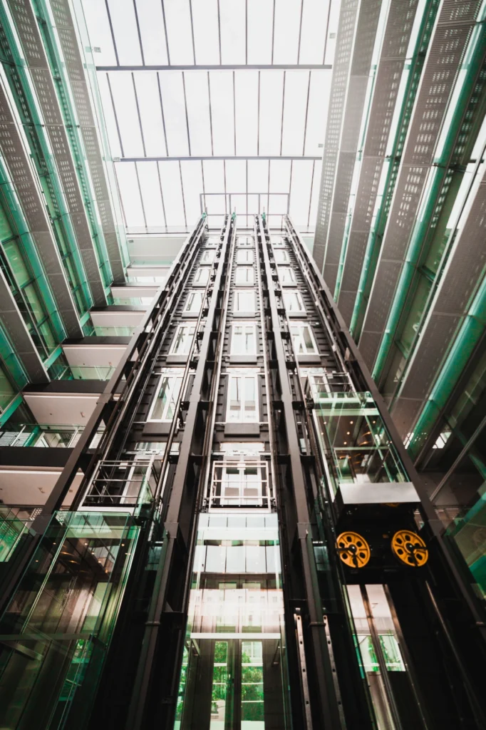 Modern glass elevators in high-rise building atrium with steel framework.