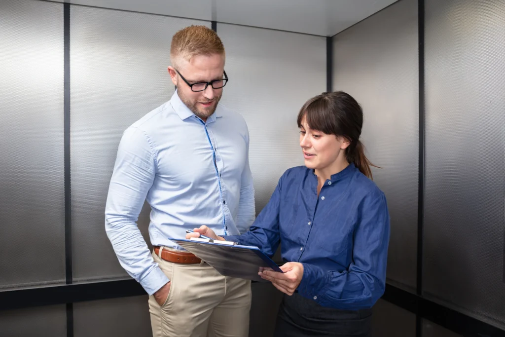 Man and woman reviewing documents inside elevator.