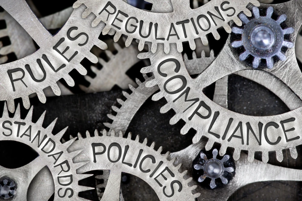 Close-up of interconnected metal gears labelled compliance, rules, and standards.
