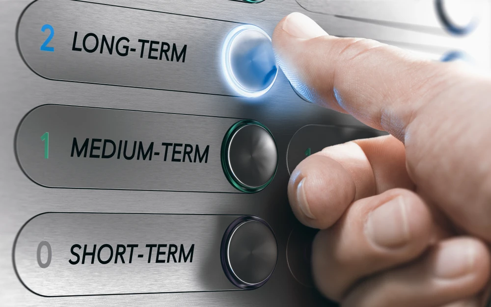 Finger pressing elevator button marked long-term for strategic asset planning.